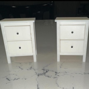May include: Two white wooden nightstands with two drawers each. The nightstands have simple, clean lines and are made of a smooth, white wood.