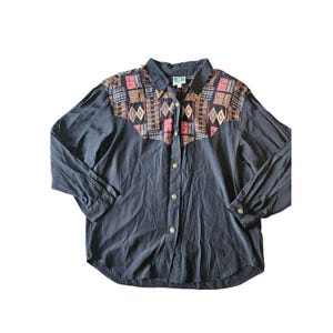 Op de afbeelding: Zwart overhemd met lange mouwen en een decoratieve pas met geometrische patronen in rood, bruin en goud. Het overhemd heeft een klassieke kraag en manchetten met knopen. De stof is zacht en soepel.