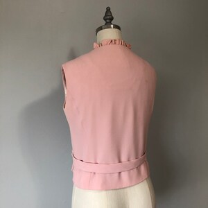 May include: A sleeveless pink vest with a ruffled neckline and a matching belt.