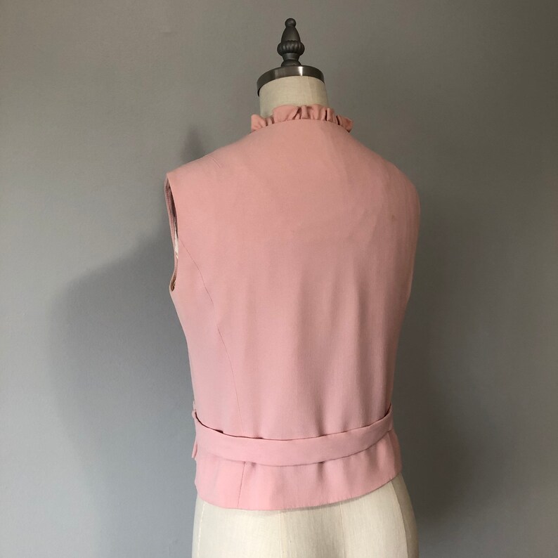 May include: A sleeveless pink vest with a ruffled neckline and a matching belt.