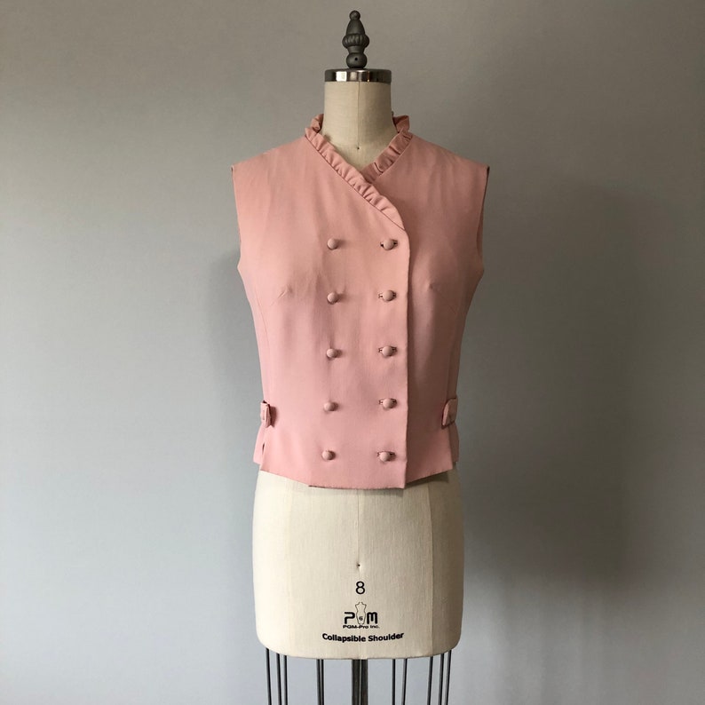 May include: A pink sleeveless vest with a ruffled collar and double-breasted button closure.