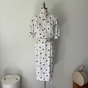 May include: A white dress with a star print and a matching belt. The stars are black and blue.