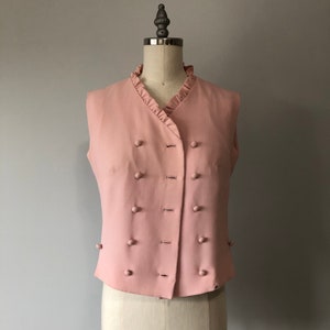 May include: A sleeveless pink vest with a ruffled collar and a double row of buttons down the front.
