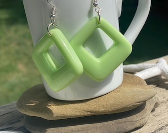 Pendientes colgantes de color verde pastel, con diseño abierto en el centro y forma de diamante moderna.