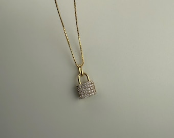 May include: A gold chain necklace with a small padlock pendant encrusted with clear cubic zirconia stones.
