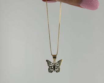 May include: A gold chain necklace with a delicate butterfly pendant. The butterfly is cut out and has a detailed design.