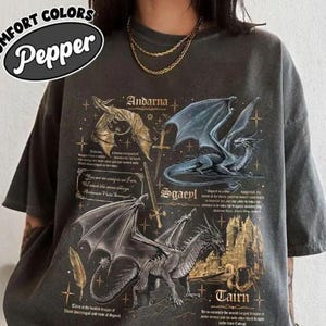 Puede incluir: Camiseta gris oscuro con tres ilustraciones de dragones y texto. La camiseta tiene un aspecto vintage, con las palabras "COMFORT COLORS" y "Pepper" en un diseño circular. Los dragones están representados en oro, azul y gris.