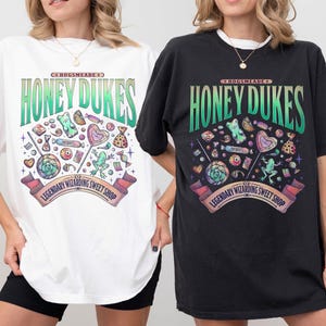 May include: White and black t-shirts with a colorful graphic design. The design features the text "Honeydukes" in green and a variety of candies and sweets. The text "Legendary Wizarding Sweet Shop" is also included.