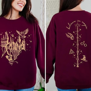 May include: Maroon sweatshirt with a gold graphic of a castle, owl, and stars on the front. The back features a wand, glasses, and the words "believe in magic" in gold. A cozy, long-sleeved top.