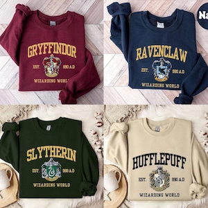 May include: Four sweatshirts, each in a different color: burgundy, navy blue, dark green, and beige. Each sweatshirt features a house name: Gryffindor, Ravenclaw, Slytherin, and Hufflepuff, with a crest and the text "Wizarding World."