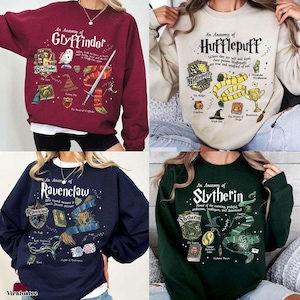 May include: Four sweatshirts, each featuring a different Hogwarts house design. The sweatshirts are burgundy, beige, navy blue, and dark green. Each design includes the house name, crest, and other related imagery. The text "An Anatomy of" is above each house name.