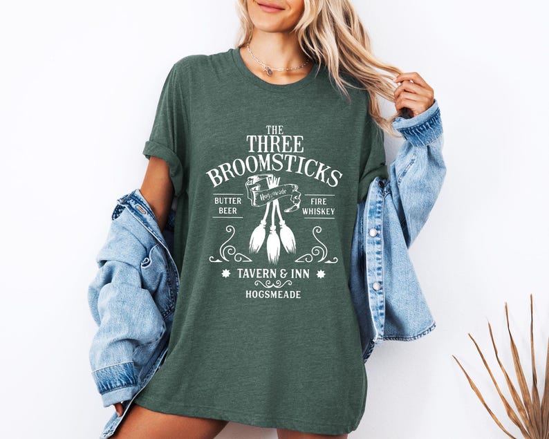 May include: A dark green t-shirt with the text "The Three Broomsticks Tavern & Inn Hogsmeade" in white. The shirt features a graphic of three broomsticks and the words "Butter Beer" and "Fire Whiskey".