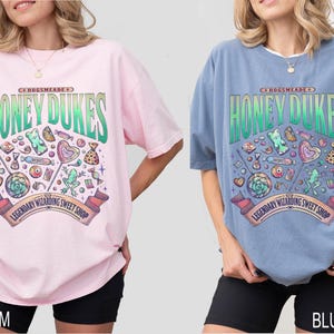 May include: Two oversized t-shirts, one pink and one blue, each featuring a graphic for Honeydukes, a legendary wizarding sweet shop. The design includes candies, lollipops, and the shop's name in a green and white font.