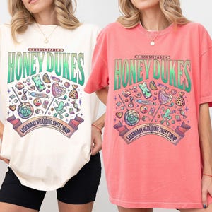 May include: Ivory and watermelon-colored t-shirts with a Honeydukes graphic. The design features the text "Honeydukes" in green, along with various candies and the text "Legendary Wizarding Sweet Shop".