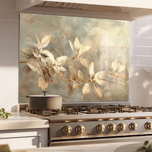 May include: A kitchen backsplash features a botanical design with gold and cream-colored leaves on a muted blue-green background. A stainless steel gas range with gold knobs is in front of the backsplash. A gray pot sits on the range.