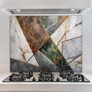 May include: A decorative kitchen backsplash with a geometric design. The backsplash features a pattern of marble-like textures in shades of gray, white, brown, and green, accented with gold lines. The backsplash is installed above a black gas cooktop.