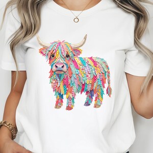 May include: White t-shirt with a colourful Highland cow illustration. The cow is made up of patchwork fabrics in pinks, blues, yellows, and greens. It has horns and a shaggy mane, giving it a whimsical, artistic appearance. The t-shirt is a casual wear item.