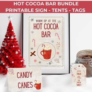 May include: A festive holiday scene featuring a red Christmas tree, a framed sign that reads "HOT COCOA BAR", and a jar of cocoa mix. Additional elements include a "Candy Canes" tent card and gift tags.