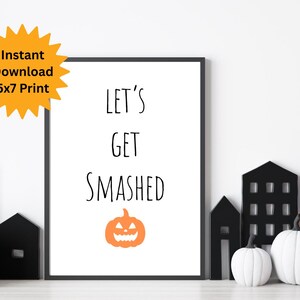 Puede incluir: Una impresión enmarcada con el texto "LET'S GET SMASHED" y una calabaza naranja. La impresión está rodeada de decoraciones de Halloween, incluyendo casas negras, calabazas blancas y un sombrero de bruja. Un gráfico de estrella amarilla dice "Descarga instantánea 5x7 Print".