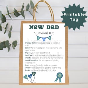 Puede incluir: Una bolsa de regalo de papel marrón con una tarjeta blanca que dice "NEW DAD Survival Kit". La tarjeta enumera elementos como bebida energética, dulces, toallitas, chupete, snacks, desinfectante de manos, chicle, patatas fritas y calcetines. Una etiqueta verde dice "Printable Tag".