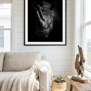 May include: A black and white framed wall art print featuring a detailed portrait of a rhinoceros head. The animal is captured in a high-contrast style against a solid black background, showcasing the textured skin and prominent horns of the rhino.