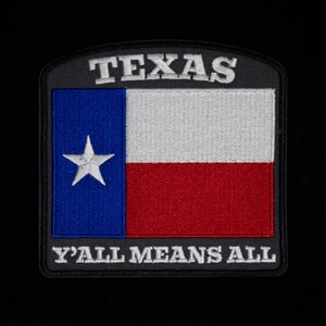 Op de afbeelding: Geborduurde patch met de vlag van de staat Texas. Het heeft een blauwe verticale streep met een witte ster, een witte streep en een rode streep. De woorden "TEXAS" en "Y'ALL MEANS ALL" zijn op de patch geborduurd.