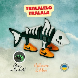 May include: A Halloween-themed shark skeleton toy with orange sneakers. The toy is black and white, with the text "TRALALELO TRALALA" above it. The image also includes the text "Glows in the dark!" and "Halloween Edition".