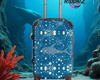May include: A blue rolling suitcase with a white dotted pattern and shark illustrations. The suitcase has a retractable handle and four wheels. The background features an underwater scene with coral and a whale. The logo "Ripplezz" is visible.