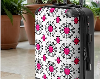 May include: Black rolling suitcase with a white background and a repeating pattern of pink ladybugs and black floral designs. The suitcase has a retractable handle and the brand name "Ripplezz" is visible.