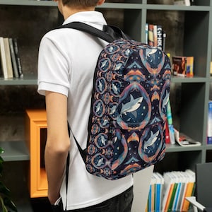 Pode incluir: Uma mochila preta com um padrão colorido de tubarões brancos e formas geométricas. A mochila tem alças ajustáveis e um fecho de correr.