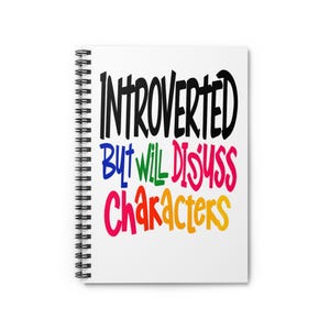 Peut inclure: Un cahier à spirales blanc avec le texte "INTROVERTED But Will Discuss Characters" en noir, bleu, vert, rose et jaune. Le cahier a une reliure à spirales noire.