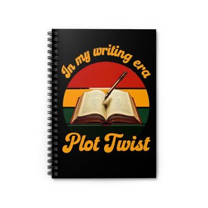 Peut inclure: Cahier à spirales noir avec le texte "In my writing era Plot Twist" en jaune et orange. Le design présente un livre ouvert avec un stylo, sur un fond rouge, orange et vert.