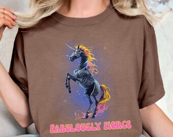 May include: Brown t-shirt featuring a skeletal unicorn design with a yellow and purple mane and tail. The text "FABULOUSLY FIERCE" is printed in pink, bubble letters below the unicorn.