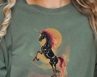 May include: Olive green t-shirt featuring a skeletal unicorn rearing up against a yellow sun. The unicorn has a pink mane and tail. The text "Magic Never Dies (It Just Gets Spooky)" is below the unicorn.