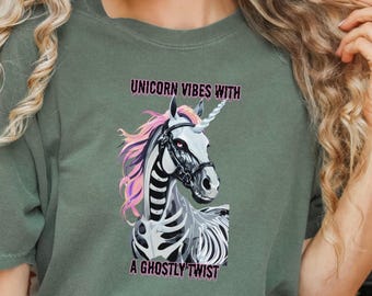 May include: Olive green t-shirt featuring a skeletal unicorn graphic with pink and white accents. The text "UNICORN VIBES WITH A GHOSTLY TWIST" is printed above and below the unicorn illustration.