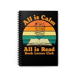 May include: Black spiral-bound notebook with the text "All is Calm All is Read Book Lovers Club" in orange and white. The design features an open book, a stylized lightbulb, and a sunset-themed background.