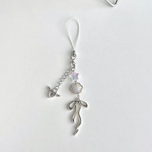 May include: A silver charm phone strap with a white and iridescent star, a white and iridescent flower, a silver heart with a keyhole, and a silver bow.
