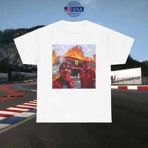 Peut inclure: T-shirt blanc avec un graphisme de deux personnes en tenue de course rouge devant un bâtiment en feu. L'image comprend le logo Ferrari et le texte "USA Best Quality" dans un design circulaire.