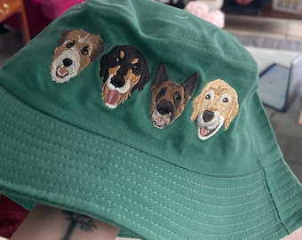 Puede incluir: Un sombrero de pescador color verde bosque con bordados detallados de cuatro caras de perro diferentes en la parte frontal. Los perros bordados incluyen un terrier de pelo duro, un perro negro y fuego, un pastor alemán y un golden retriever.