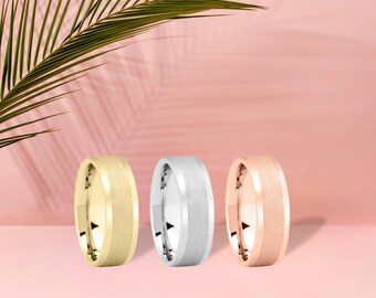 May include: Three wedding bands in gold, silver, and rose gold are displayed against a pink background. The bands have a textured finish. The text "10K-14K-18K" is at the bottom of the image.