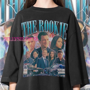May include: Black t-shirt featuring a graphic of the TV show "The Rookie." The design includes the show's title in blue and images of the cast, along with police cars. The shirt has a vintage, distressed look.