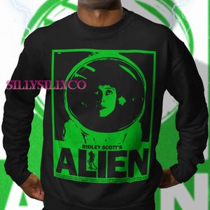 Pu&ograve; includere: Felpa nera con grafica verde di Alien di Ridley Scott. La grafica include un ritratto di una donna con un casco spaziale e il titolo del film. La felpa ha il testo "SillySillyCo" sul lato sinistro.