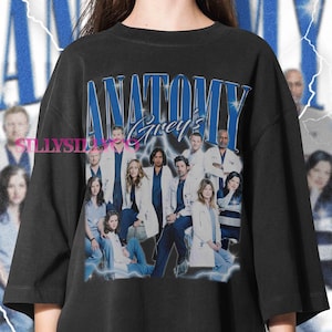 May include: Black oversized t-shirt featuring a group photo of the cast of Grey's Anatomy, with the show's title in blue and white lettering. The design includes a lightning bolt effect, creating a vintage aesthetic.