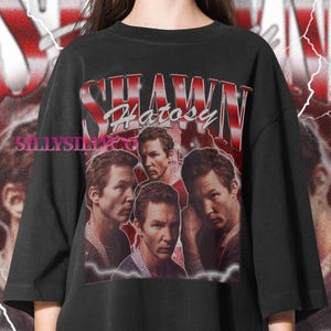 Könnte beinhalten: Schwarzes übergroßes T-Shirt mit einer Grafik von Shawn Hatosy und dem Namen "Shawn Hatosy" in Rot und Weiß. Das Design hat einen Vintage-Look mit einem verblichenen Hintergrund.
