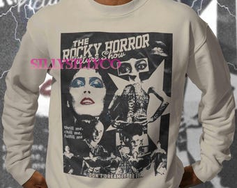 Puede incluir: Una sudadera crema con un gráfico en blanco y negro de "The Rocky Horror Picture Show". El diseño incluye el título de la película, imágenes de personajes y la frase "DON'T DREAM IT BE IT."
