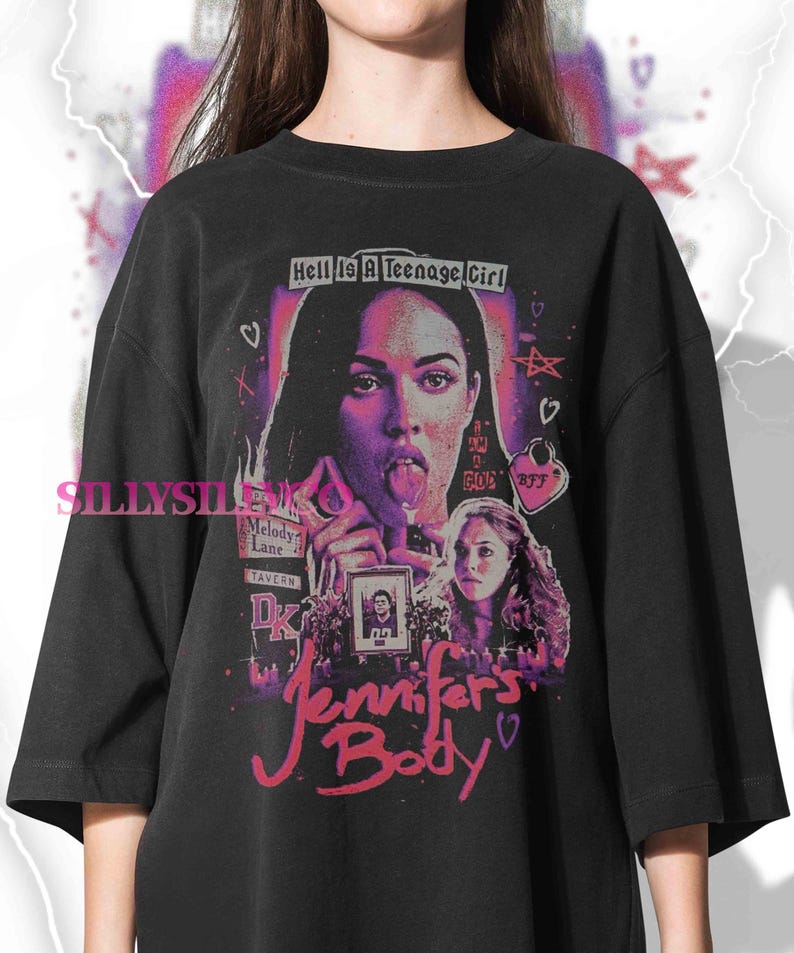 May include: Black oversized t-shirt featuring a graphic design from the movie "Jennifer's Body." The design includes a portrait of a woman with her tongue out, the text "Hell Is A Teenage Girl," and the movie title in pink script.