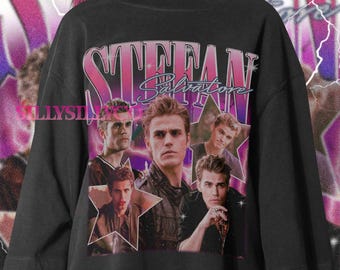 May include: Black t-shirt featuring a collage of images of a person with the text "STEFAN SALVATORE" in a pink and purple retro font. The design includes star shapes and a vintage aesthetic.
