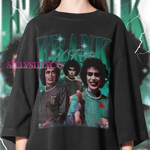 May include: Black t-shirt with a graphic of Frank N. Furter from The Rocky Horror Picture Show. The design features the name "Frank N Furter" in green and blue, with three images of the character. The shirt has a vintage, distressed appearance.