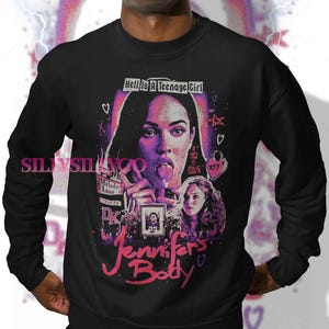 May include: Black sweatshirt featuring a graphic from the movie "Jennifer's Body." The design includes a portrait of a woman with her tongue out, the text "Hell Is A Teenage Girl," and the movie title in pink script.