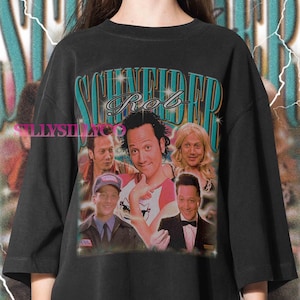 May include: Black t-shirt featuring a graphic of Rob Schneider with the text "Schneider Rob" in a retro design. The graphic includes multiple images of the actor. The shirt has a vintage, worn look.